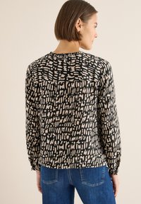 Musta-beige pitkähihainen pusero, jossa abstrakti kuvio, pyöreä kaula-aukko, rento istuvuus ja kootut yksityiskohdat hihansuuissa.