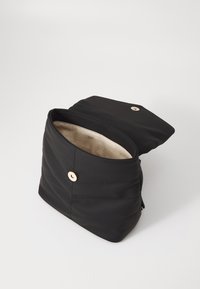 Zwarte gewatteerde nylon tas met een omslagflap en een gouden knoopsluiting. Interieur gevoerd met lichte stof met een gedrukt logo.