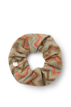 Coletero de tela con un patrón de zigzag texturizado en tonos verdes apagados, naranja y marrón, con una pequeña etiqueta metálica redonda.