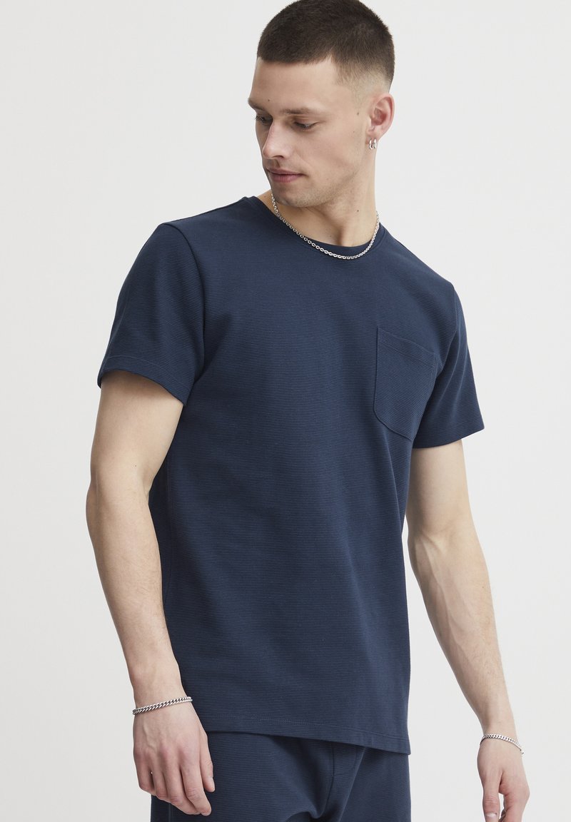 Tricou din bumbac bleumarin cu guler rotund, realizat dintr-un material texturat, având mâneci scurte și un buzunar pe pieptul stâng. Croială casual cu linii curate.