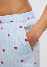Shorts rayés bleu clair avec petite broderie de fraise rouge ; dotés d'un tissu doux, d'une ceinture élastique et d'un détail de poche latérale.