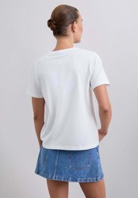 Biała bawełniana koszulka z krótkim rękawem, prosto zakończona, noszona z niebieską dżinsową spódnicą mini z kieszeniami i lekko rozszerzanym kształtem.