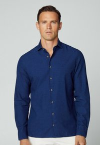 Camicia button-up blu navy in tessuto di cotone, con colletto a punta, maniche lunghe e taschino frontale discreto. Bottoni in tono ottone accentuano il design.