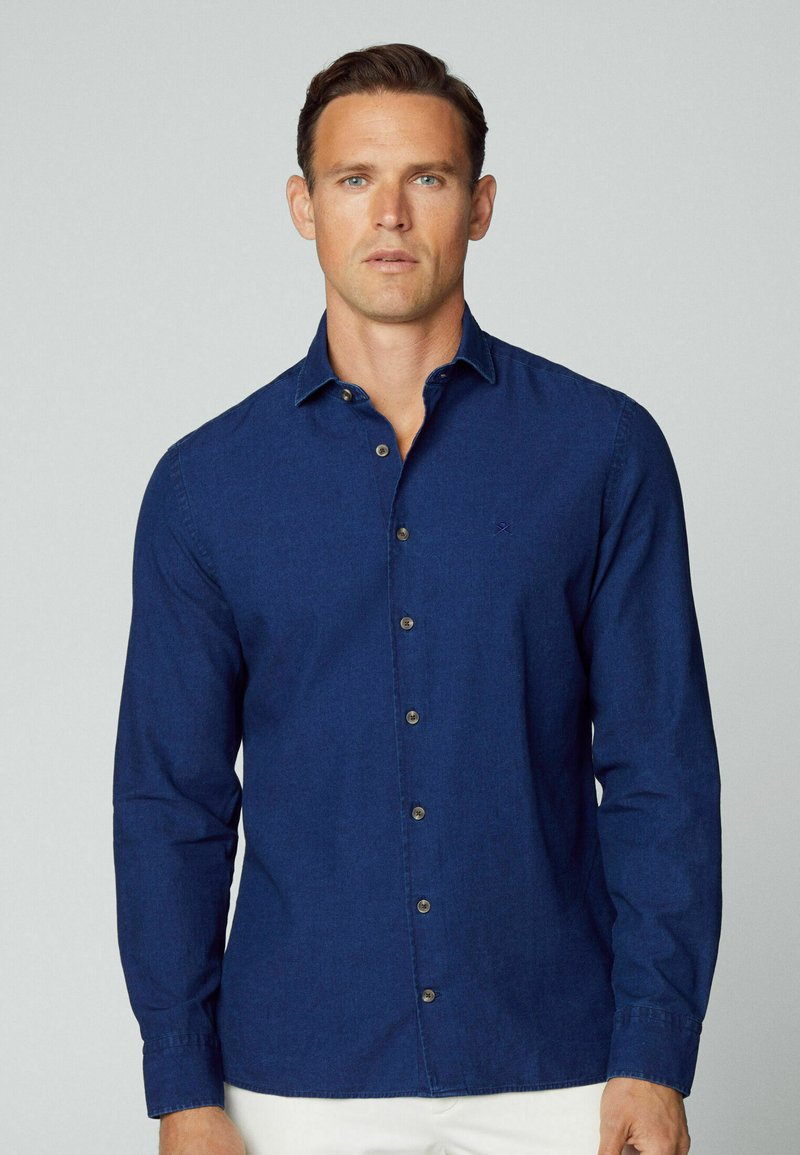 Camicia button-up blu navy in tessuto di cotone, con colletto a punta, maniche lunghe e taschino frontale discreto. Bottoni in tono ottone accentuano il design.