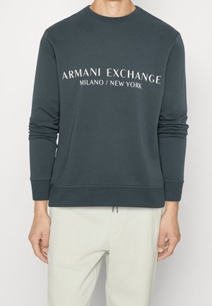 Sudadera de color verde oscuro con cuello redondo, mangas largas y puños acanalados; presenta el texto blanco "Armani Exchange Milano/New York" en la parte frontal.
