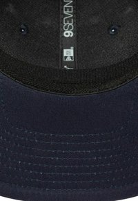 Cappellino da baseball blu navy con visiera curva, realizzato in tessuto testurizzato. Presenta una banda interna nera e cuciture blu lungo il bordo. Etichetta visibile.