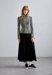 Haut à manches longues à rayures noires et blanches, jupe maxi plissée noire, associée à des baskets noires et des chaussettes blanches. Tissu texturé, design ajusté.