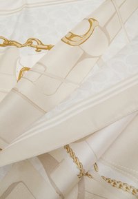 Silke tørklæde med en beige baggrund og gyldne kæde- og accentmønstre. Glat tekstur med en foldet kant, der fremviser intrikate design detaljer.