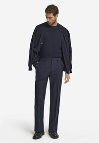 Marinblå ullkardigan över en marinblå texturerad tröja, kombinerad med skräddarsydda mörka byxor och svarta läderskor. Enkla, rena linjer och knappar.