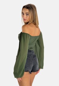 Top verde in chiffon a spalle scoperte con maniche lunghe, abbinato a pantaloni corti in denim grigi strappati a vita alta. Vista posteriore mostrata.