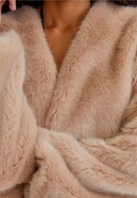 Faux fur-wrap i mjuk beige, med en lyxig textur och breda, vinklade slag. Tyget har en subtil glans och faller elegant.