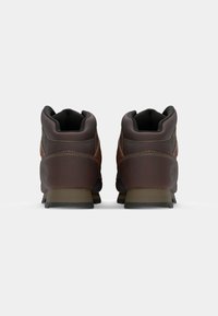 Botas de tobillo de cuero marrón con un acabado suave, puntas redondeadas, cuellos acolchados y suelas de goma negras; cuenta con un detalle de costura en contraste.