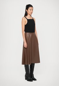 Black sleeveless top paired with a brown faux leather midi skirt. Black knee-high boots with a chunky heel complete the outfit.