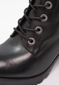 Bota de cuero negra con ojales metálicos, cordones gruesos negros, un acabado suave y un diseño de suela resistente con patrones de tracción.