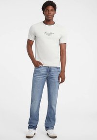 Lysegrå bomuld t-shirt med korte ærmer og rund hals, med 'Guess Jeans' logo i skrift. Kombineret med falmet blå denim jeans.