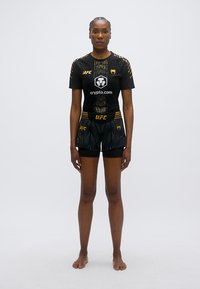 Črna športna uniforma UFC z kratkimi rokavi in kratkimi hlačami, z zlatimi poudarki, vključno z logotipi in mrežasto teksturo.