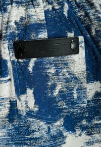 Tela de patrón azul y blanco con un tejido texturizado, que presenta una etiqueta de cuero negro con texto en relieve y dos botones a presión.