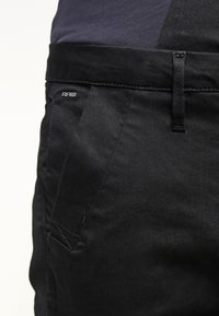 Czarne spodnie wykonane z bawełny o gładkiej fakturze. Posiadają elastyczny pas z logo oraz przednią kieszeń z ukośnym przeszyciem.