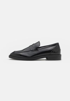 Mocassins en cuir noir à finition lisse avec un détail de couture surélevée à l'avant. Ils présentent un petit talon carré et un bout arrondi.