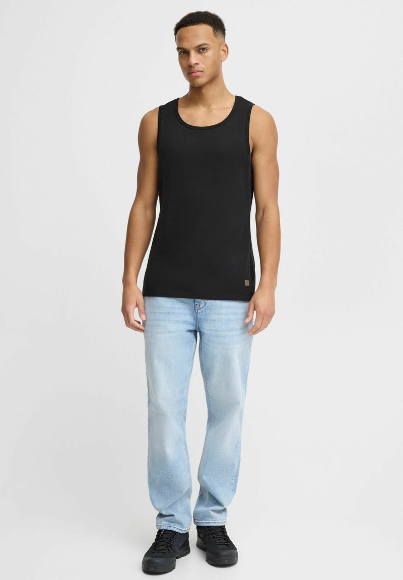 Top in cotone nero senza maniche con scollatura rotonda, indossato con jeans in denim azzurro chiaro e scarpe da ginnastica nere. Nessun motivo o logo visibili.