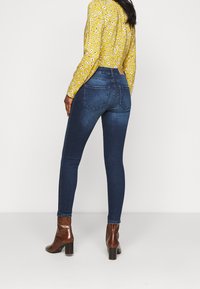 Mörkblå skinny jeans i denim med hög midja, som har en klassisk femficksdesign och subtila detaljer på bakstycket, ihop med bruna klackstövlar.