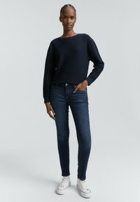 Pull en maille bleu marine avec un col rond, associé à un jean slim noir et des baskets blanches, présentant un design et une texture classiques.