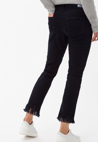 Jeans de mezclilla azul oscura con dobladillo deshilachado, ajuste slim y bolsillos traseros, combinados con zapatillas blancas. Tejido texturizado con elasticidad.