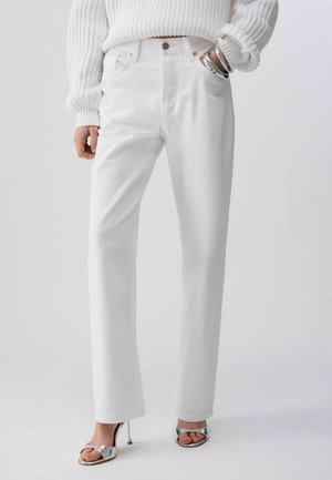 Osoba oblečená v bílých vysokým pasem, rovnými džíny, bílém žebrovaném svetru, stříbrných náramcích a stříbrných sandálech s otevřenou špičkou.