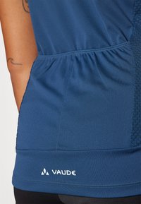 Blå treningscroppe laget av glatt stoff med rynket midje og teksturert sidepanel. Hvit "Vaude"-logo nær sømmen.