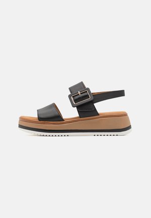 Black leather platform sandal with two wide straps, adjustable buckle, and a layered brown and white sole. Textured tread details on bottom.