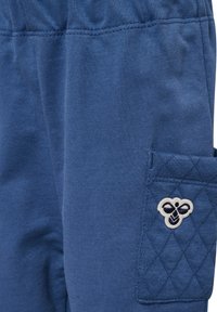 Blå tygbyxben med elastisk midja och vadderad sidoficka med en liten broderad bi-design.