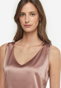 Satynowa koszulka w delikatnym odcieniu różu, z dekoltem w kształcie litery V i cienkimi ramiączkami. Gładka tekstura z lekkim połyskiem i minimalistyczny design.