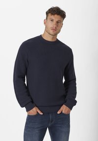 Marineblauer Strickpullover mit einem strukturierten Muster, ausgestattet mit einem gerippten Rundhalsausschnitt, langen Ärmeln und einem horizontal gestreiften Abschnitt, kombiniert mit Jeans.