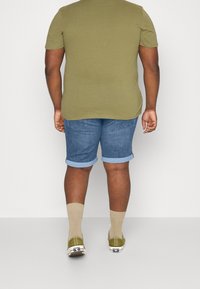 Olive green short-sleeve t-shirt, light blue denim shorts with rolled cuffs, beige socks, and green shoes, viewed from the back.