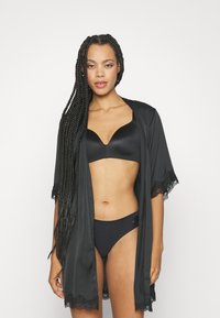 Crni satenasti kimono s čipkastim rubom, otvorenog prednjeg dijela i kratkim rukavima, nošen preko crnog grudnjaka i bikinija. Glatka tekstura i minimalistički dizajn.
