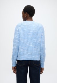 Γαλάζιο πλεκτό πουλόβερ με υφή, στρογγυλή λαιμόκοψη και ριμπ τελείωμα. Φοριέται με σκούρο μπλε τζιν σε ουδέτερο φόντο.