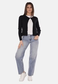 Cardigan nero in tessuto lavorato a maglia, con apertura frontale, maniche lunghe, abbinato a jeans di cotone azzurri e sneakers bianche.