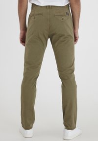 Olive zelené chino kalhoty se střihem rovné nohy, vyrobené z měkké bavlny. Mají zadní kapsy na knoflíky a poutka na pásek. Nošeny s bílými teniskami.