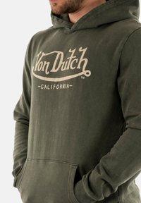 Sweat à capuche vert olive avec une poche avant, des poignets côtelés et un logo blanc usé "Von Dutch CALIFORNIA" sur la poitrine.