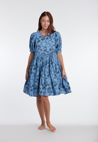 Plava haljina napravljena od lagane tkanine s crnim cvjetnim uzorkom. Ima napuhane rukave i nabranu suknju. Elegantnog je i lepršavog dizajna.