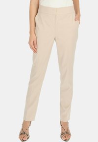 Jasno beżowe dopasowane spodnie o gładkiej fakturze, wysoki krój, z płaskim pasem. Zawierają boczne kieszenie i są zestawione z sandałami na paski.