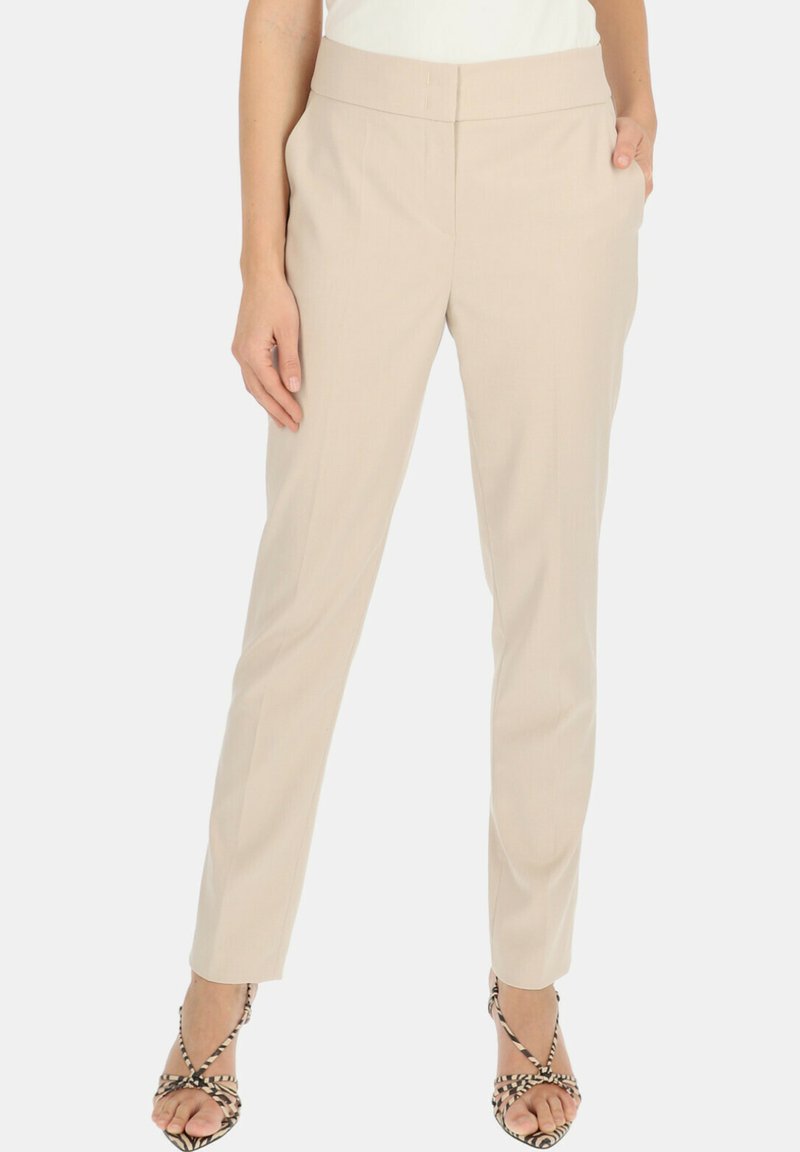 Jasno beżowe dopasowane spodnie o gładkiej fakturze, wysoki krój, z płaskim pasem. Zawierają boczne kieszenie i są zestawione z sandałami na paski.
