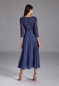 Abito da sera blu navy con corpetto in pizzo, maniche a tre quarti e gonna fluida. Presenta una vita aderente e una trama di tessuto morbido.