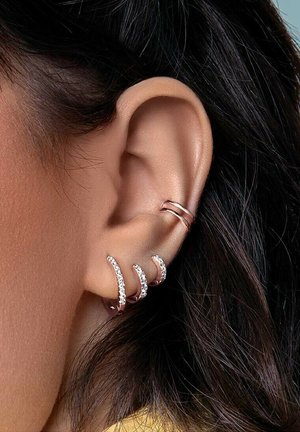 Drei Ohrcuffs aus Roségold mit geschwungenen Designs und eingelassenen klaren Strasssteinen verzieren das äußere Ohr. Glatte Oberfläche auf der metallischen Struktur.