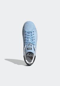 Ljusblå mocka sneakers har platta snören, en vit gummisula, svarta accenter vid hälen och en tagg med varumärkets logotyp på tungan.