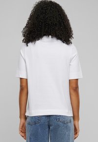 Weißes Kurzarm-T-Shirt mit Rundhalsausschnitt, aus weichem Baumwollmaterial gefertigt, mit einem lässigen Schnitt und geradem Saum, kombiniert mit blauen Jeans.