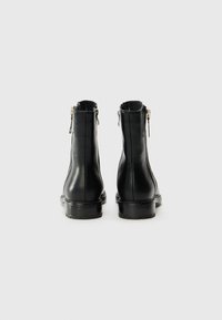 Botas de tobillo de cuero negro con un acabado suave, que cuentan con cremalleras laterales y una suela de goma plana. Diseño minimalista con detalles de costura.