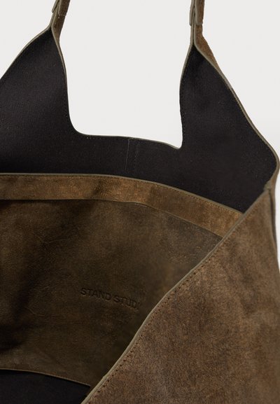 Geantă tote maro din piele întoarsă cu textură moale, având o deschidere largă și captuseală din pânză neagră. Inscripția "STAND STUDIO" este embosată în interior.
