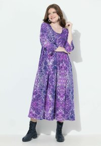 Robe maxi violette avec un motif marbré, manches 3/4 et encolure ronde. Associée à des bottes noires à lacets. Texture de tissu lisse.