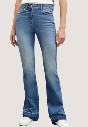 Blue denim flared jeans with a high waist, fading on thighs, and frayed hems. Worn with white sneakers and a plain white top.